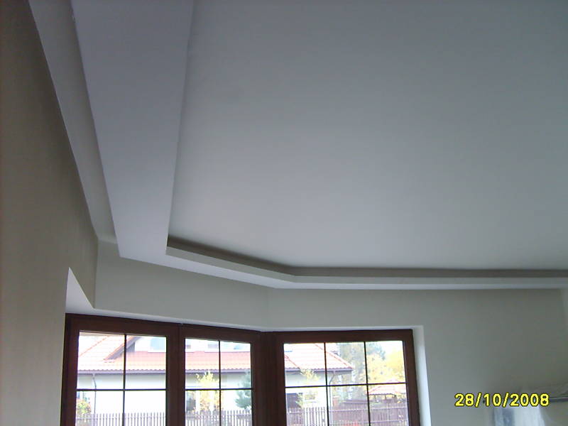 Pomieszczenie po adaptacji poddasza: widok na gładki, biały sufit z dekoracyjnymi obniżeniami i oknem w tle.