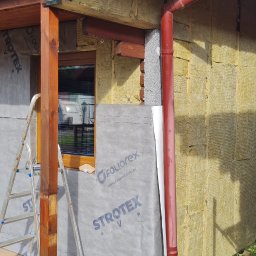DAW-BUD Zakład Remontowo Budowlany Zabrzeski Dawid - Budynek w trakcie ocieplania elewacji: widoczna warstwa izolacji z wełny mineralnej, folia paroizolacyjna z nadrukiem 'STROTEX' i 'FOLIOREX', drewniana stolarka okienna i drzwiowa, oraz fragment...