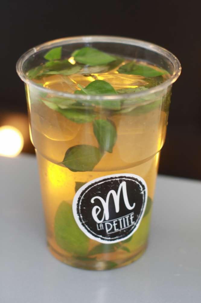 Napój w przezroczystym kubku z liśćmi mięty i naklejką 'La Petite', ustawiony na jasnej powierzchni.