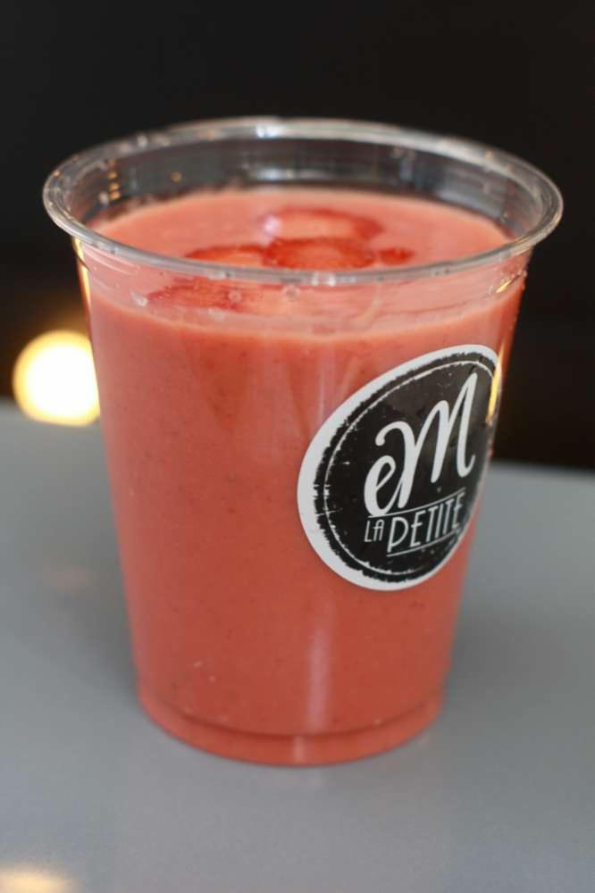 Różowy koktajl truskawkowy w plastikowym kubku z naklejką logo firmy, udekorowany plasterkami truskawek na wierzchu.