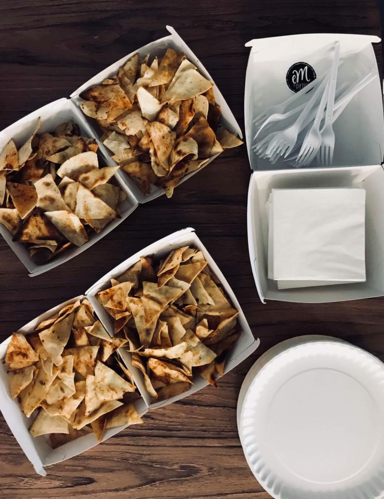 Cztery białe kartonowe pojemniki z trójkątnymi chipsami, serwetkami i plastikowymi widelcami na drewnianym stole, gotowe do spożycia.