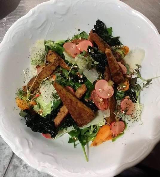 Apetyczna sałatka z grillowanymi warzywami korzeniowymi, rzodkiewką, świeżymi ziołami i posypką z czarnego pieprzu, podana w ozdobnej, białej misce.