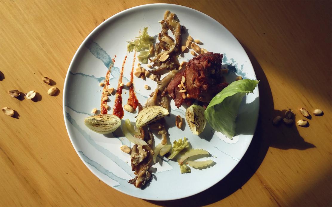 Elegancko podane danie mięsne z warzywami, orzechami i sosem na talerzu z delikatnym, niebieskim wzorem, oświetlone naturalnym światłem.