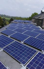 Panele słoneczne na dachu budynku jednorodzinnego, widok z góry, lekko pochmurne niebo w tle.