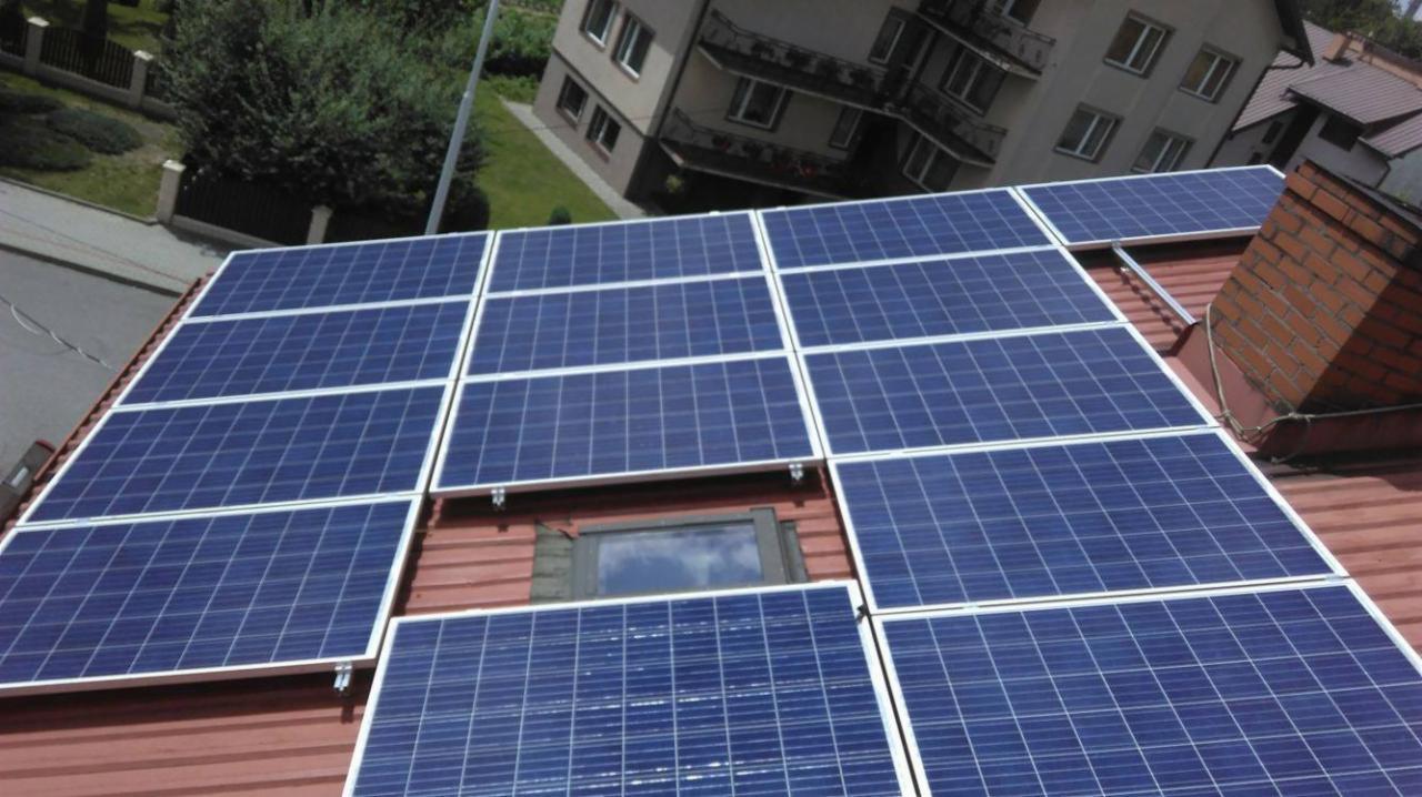 Instalacja paneli słonecznych na dachu domu z ceglanym kominem i oknem dachowym, widok z góry.