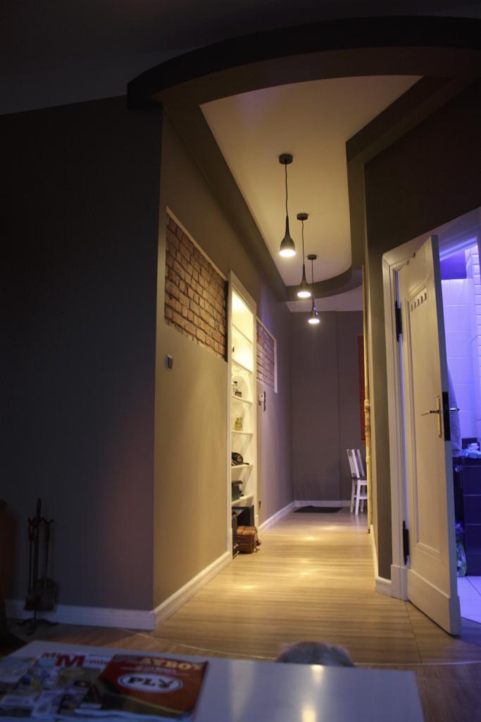 Korytarz po remoncie w Toruniu z oświetleniem punktowym, fragmentem ściany z cegły i zabudowaną szafą.