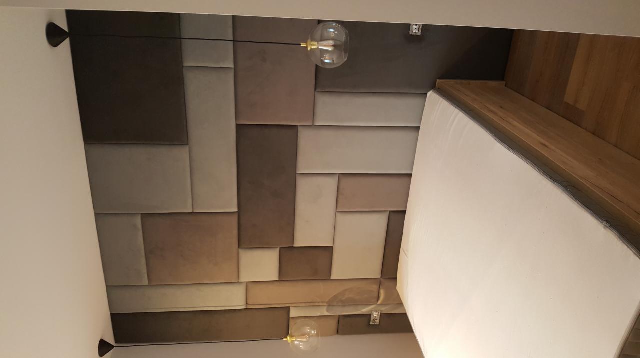 Panel tapicerowany na ścianie w sypialni, z lampami wiszącymi, widok z dołu na wezgłowie łóżka i fragment drewnianej podłogi.