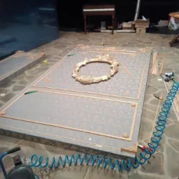 Przygotowywane dekoracyjne panele ścienne z ornamentami i ramką w stylu klasycznym, narzędzia stolarskie w tle, podłoga z kamiennych płyt.