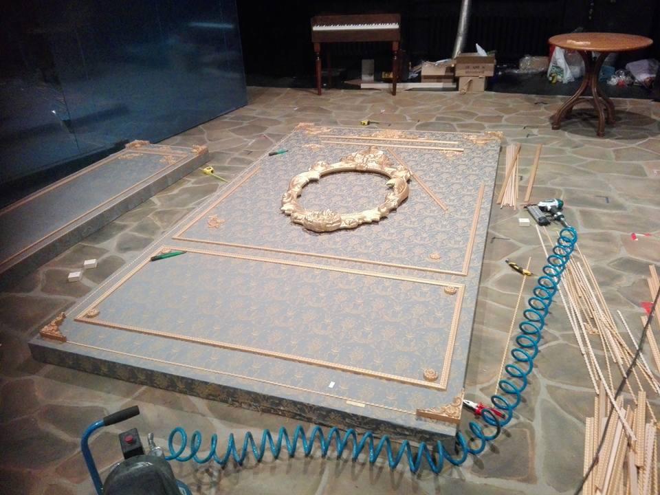Przygotowywane dekoracyjne panele ścienne z ornamentami i ramką w stylu klasycznym, narzędzia stolarskie w tle, podłoga z kamiennych płyt.