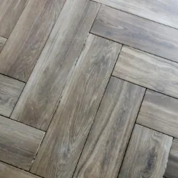 Ułożone panele podłogowe w jodełkę, z widoczną strukturą drewna i subtelnymi przebarwieniami, z bliska, z drobnymi defektami na powierzchni.