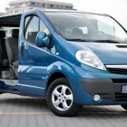 Niebieski Opel Vivaro Tour z otwartymi drzwiami przesuwnymi na tle nowoczesnego budynku.