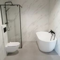 Nowoczesna łazienka z białą armaturą: wisząca toaleta, owalna wanna z czarną baterią i kabina prysznicowa z czarną ramą na tle marmurowych płytek.