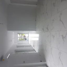 Wnętrze z nową, białą marmurową podłogą z płytek, widoczne okna i klimatyzator na ścianie, instalacja elektryczna w trakcie prac.