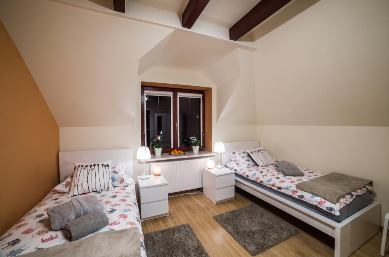 Pokój z dwoma łóżkami w Grodzisku Mazowieckim, z oknem na poddaszu, drewnianymi belkami stropowymi i lampkami nocnymi na białych szafkach.