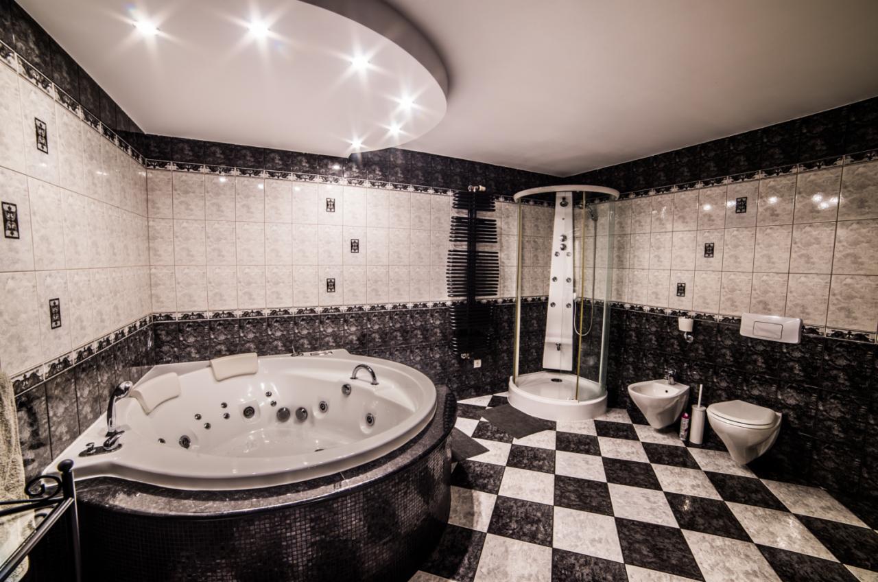 Nowoczesna łazienka z okrągłą wanną z hydromasażem, kabiną prysznicową ze szklanymi drzwiami, bidetem i toaletą na podłodze w szachownicę.