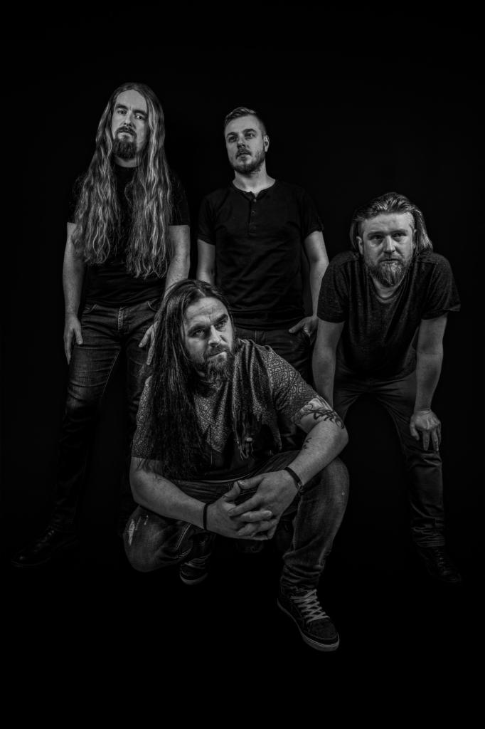 Czarno-białe portretowe ujęcie zespołu muzycznego w studyjnym oświetleniu, lider zespołu w przysiadzie z tatuażem na ramieniu.