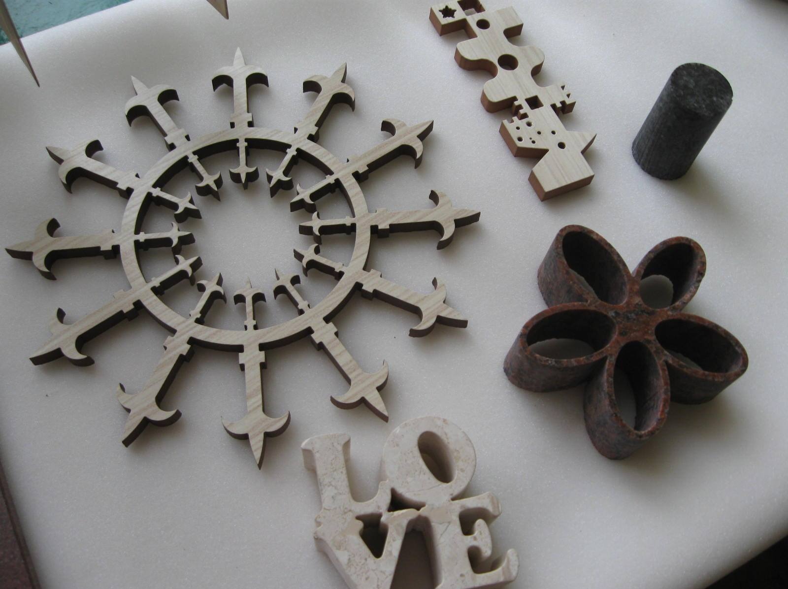 Precyzyjnie wycięte laserowo drewniane i kamienne elementy dekoracyjne: ażurowa rozeta, puzzle, cylinder i kwiat. Jasne drewno kontrastuje z ciemnym obrysem.