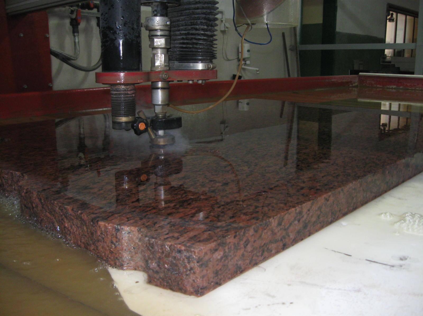 Cięcie wodą czerwonego granitu na maszynie CNC. Obróbka kamienia z bliska, widoczne chłodzenie wodne i dysza tnąca. Precyzyjna obróbka materiału.