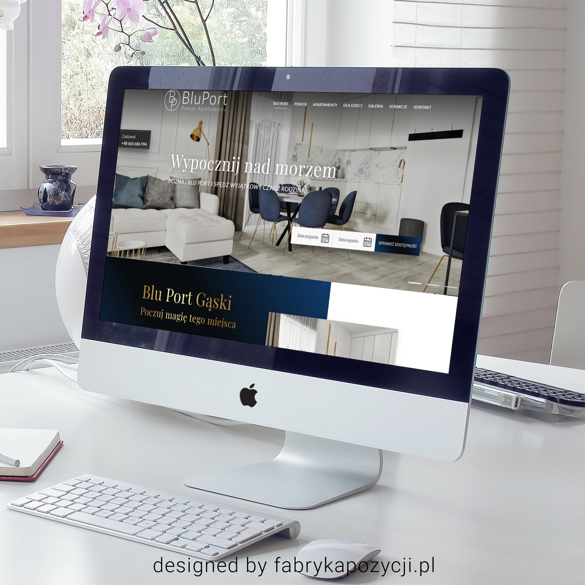 Ekran komputera iMac wyświetlający stronę internetową BluPort Pokoje Apartamenty Gąski, obok klawiatura Apple, myszka i notatnik na białym biurku, w tle okno z kwiatami.
