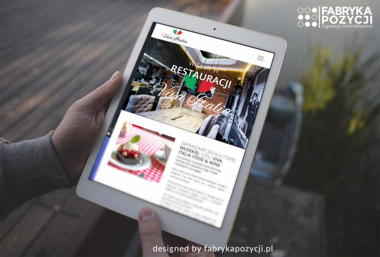 Tablet prezentuje stronę internetową restauracji Viva Italia z elementami menu i logo, trzymany w dłoni na tle drewnianej powierzchni.