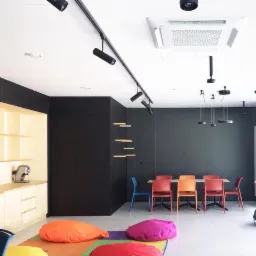 Nowoczesne wnętrze biurowe z klimatyzacją kasetonową, oświetleniem szynowym i kolorowymi pufami na podłodze.