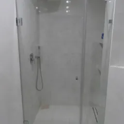 Szklana kabina prysznicowa z chromowanymi zawiasami i deszczownicą, widok z zewnątrz, białe płytki na ścianach i podłodze, logo firmy Baccarat w rogu.