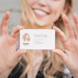 Kobieta uśmiechnięta, trzymająca wizytówkę salonu kosmetycznego 'Salon Beaty' na tle rozmytej twarzy i ceglanej ściany.