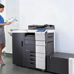 DKS Sp. z o.o. Oddział Kraków - Kobieta przegląda dokumenty obok nowej, wielofunkcyjnej kserokopiarki A3 w nowoczesnym biurze z roślinami doniczkowymi.