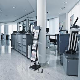 DKS Sp. z o.o. Oddział Kraków - Przestronne biuro z rzędem wielkoformatowych kserokopiarek i stojakiem na ulotki, widok na marmurową podłogę i kolumnę.