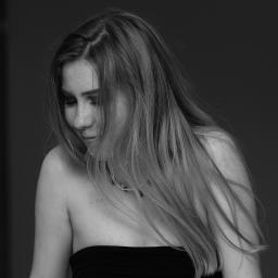 Tomasz Krzyczkowski - Portret w czerni i bieli: Młoda kobieta z długimi włosami spogląda w dół, nosząc czarną sukienkę bez ramiączek i delikatny naszyjnik.