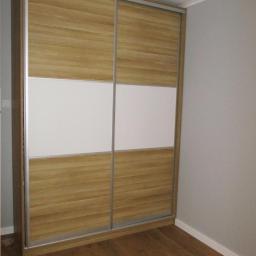 MM-Design - Dwudrzwiowa szafa przesuwna z panelami z drewna i białymi wstawkami, widoczna na tle szarej ściany i drewnianej podłogi.