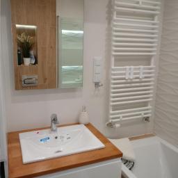 MM-Design - Nowoczesna łazienka z białą umywalką Diverta na drewnianym blacie, szafką pod umywalką, lustrem z półkami i grzejnikiem drabinkowym.