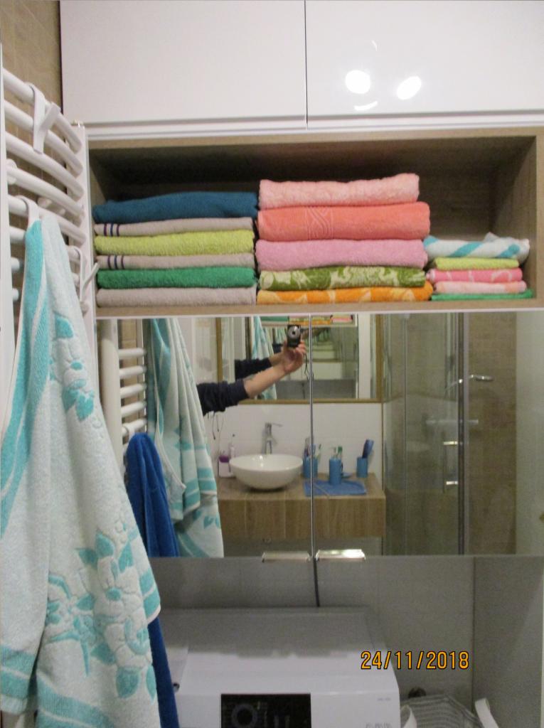 Półka z ręcznikami w łazience, widoczna w lustrzanym odbiciu podczas robienia zdjęcia.