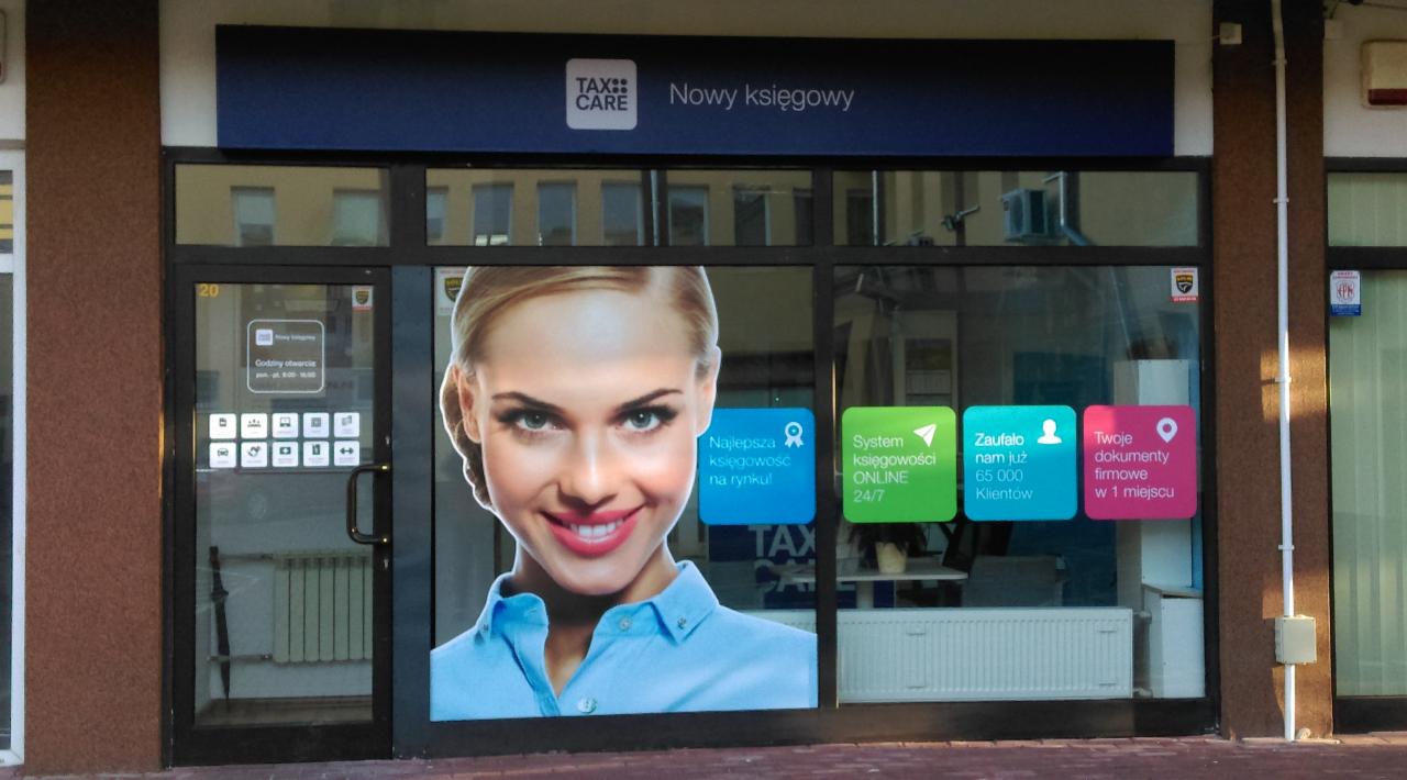 Fasada budynku z naklejkami reklamowymi firmy świadczącej usługi finansowe, widoczna grafika kobiety i hasła o księgowości online oraz zaufaniu klientów.