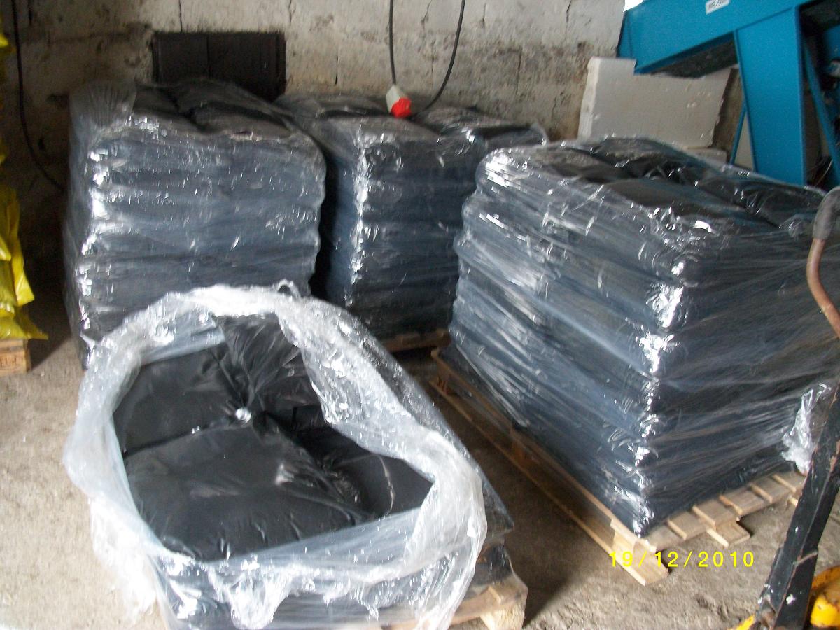 Stosy workowanego opału w czarnych foliach, ułożone na paletach w magazynie, widoczne z bliska, z datą na dole zdjęcia.