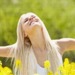 Blond kobieta z rozłożonymi rękami, głęboko oddycha w kwitnącym polu rzepaku, odczuwając ulgę i swobodę.