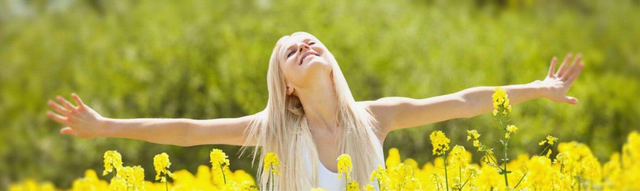 Blond kobieta z rozłożonymi rękami, głęboko oddycha w kwitnącym polu rzepaku, odczuwając ulgę i swobodę.