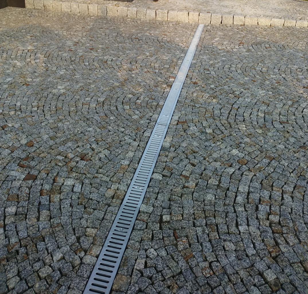 Ułożona kostka granitowa w łukowaty wzór z liniowym odpływem wody na środku, widok z góry.