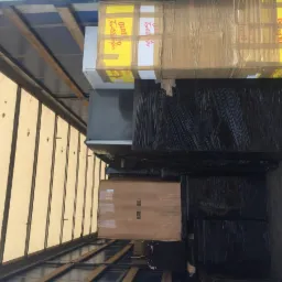 Wnętrze ciężarówki załadowane różnymi przedmiotami, w tym kartonami z napisem 'MADE IN ITALY', lodówką i meblami owiniętymi czarną folią stretch.