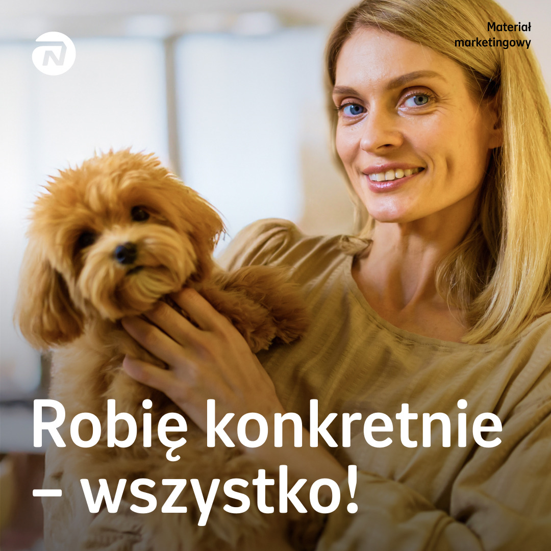Uśmiechnięta kobieta z blond włosami trzymająca na rękach małego, rudego pieska w Śremie. Materiał marketingowy.