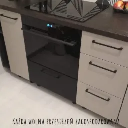 Fragment zabudowy kuchennej z piekarnikiem i szufladami w kolorach beżowym i czarnym, widok z niskiej perspektywy.