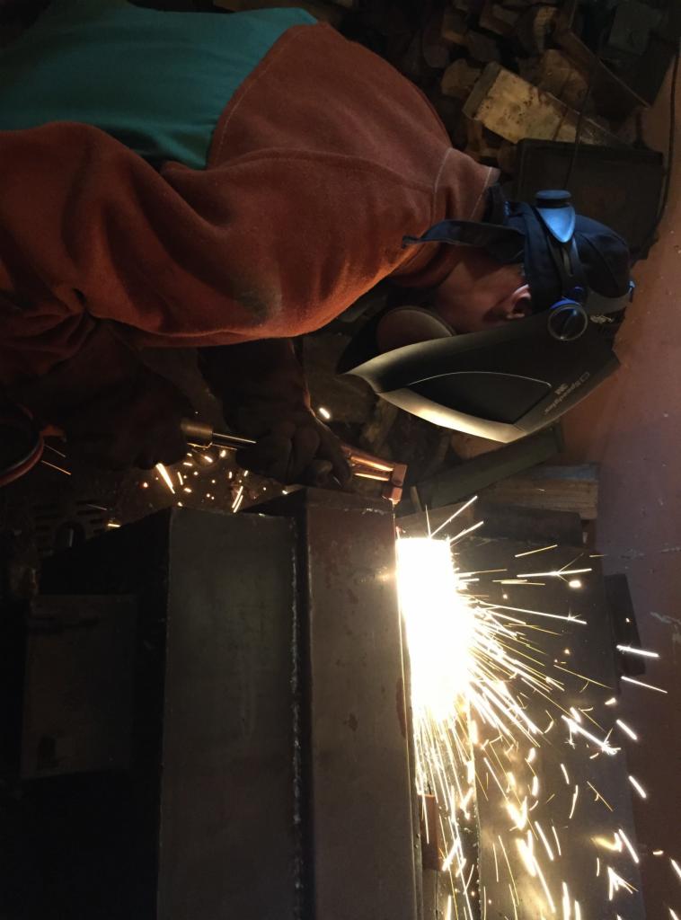 Pracownik w masce spawalniczej 3M spawający metalowe elementy konstrukcyjne, widoczne iskry.