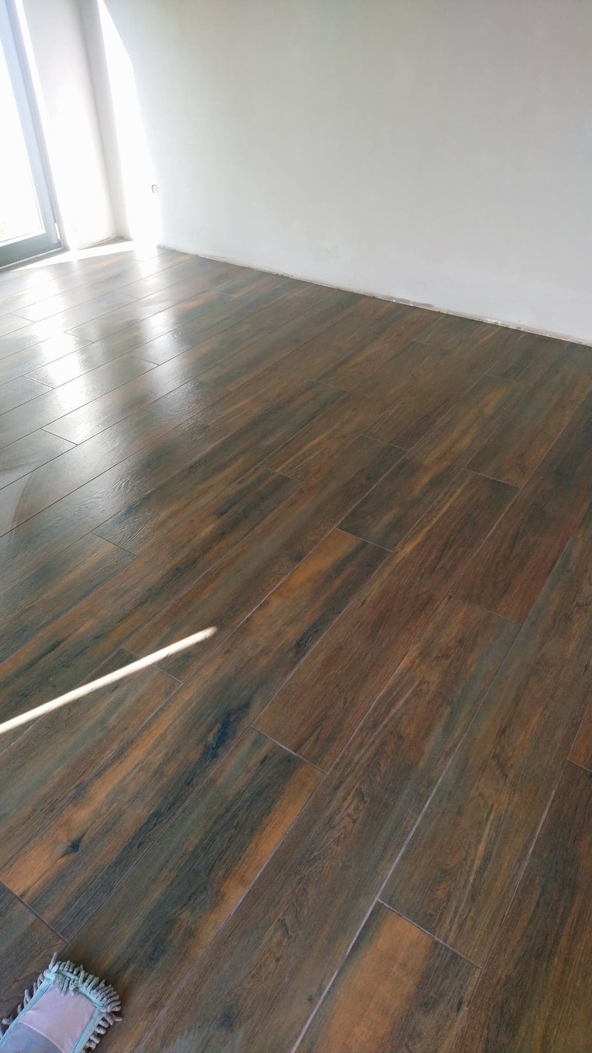 Ułożona, brązowa glazura imitująca drewno w Bydgoszczy, świeżo po umyciu, z widocznym fragmentem mopa w rogu.