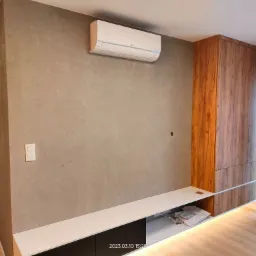 Szara ściana z dekoracyjną strukturą, zamontowany klimatyzator LG, wbudowana szafka z drewnopodobnym fornirem, biało-czarna szafka RTV z podświetleniem LED na podłodze z paneli.