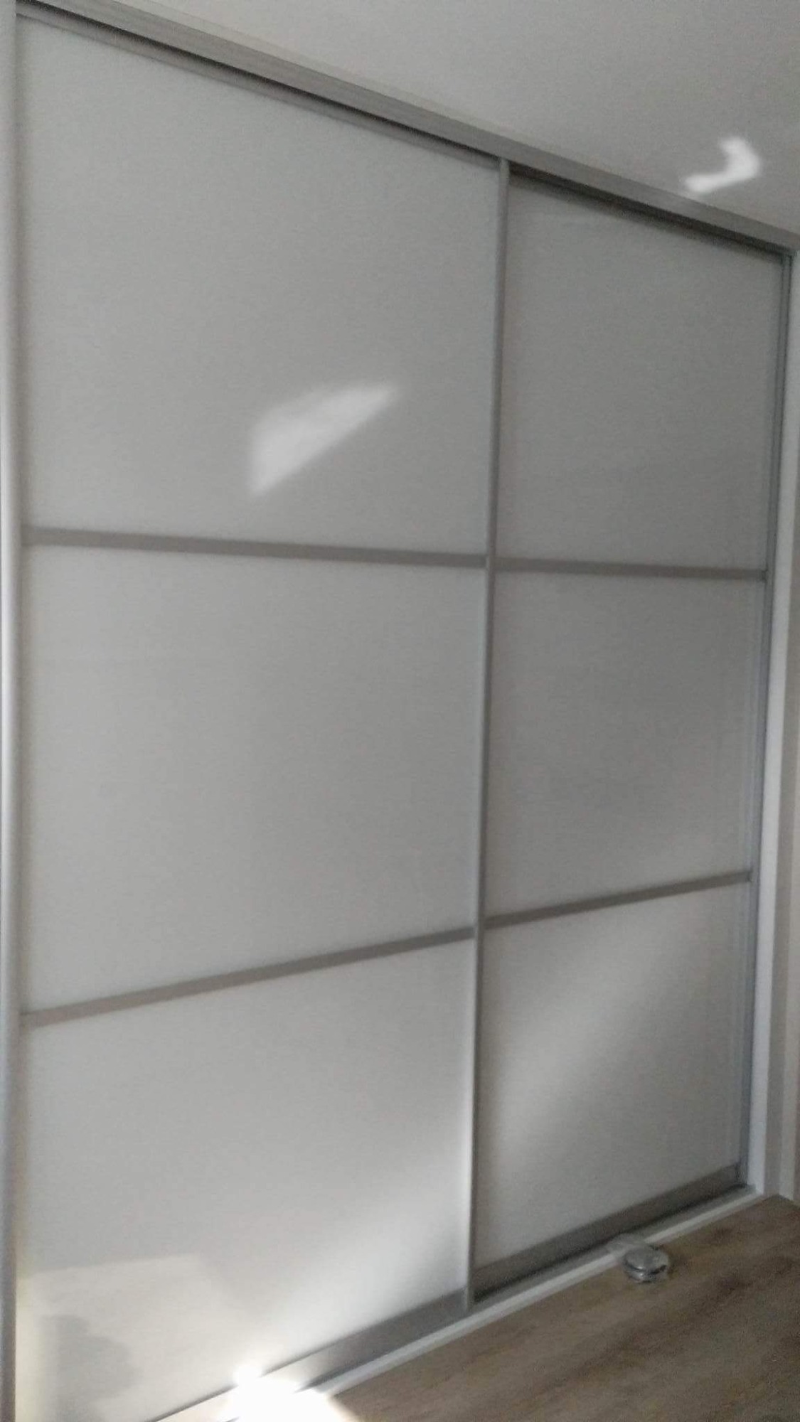 Biała szafa przesuwna z sześcioma panelami i srebrnymi ramami, widoczna na tle jasnej podłogi.