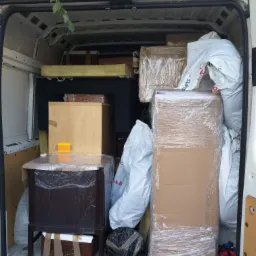 Wnętrze białego busa wypełnione meblami i przedmiotami zabezpieczonymi folią stretch i taśmą, gotowe do transportu.