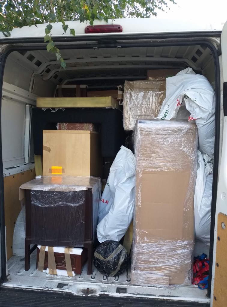Wnętrze białego busa wypełnione meblami i przedmiotami zabezpieczonymi folią stretch i taśmą, gotowe do transportu.