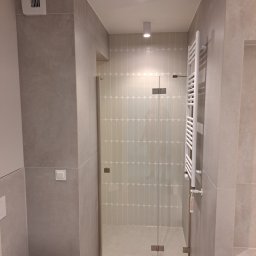 Wojewoda Jakub - Nowoczesna łazienka w odcieniach szarości z kabiną prysznicową ze szklanymi drzwiami na zawiasach, grzejnikiem drabinkowym i płytkami w kształcie migdałów na ścianie wewnątrz kabiny.