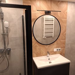 Wojewoda Jakub - Nowoczesna łazienka we Wrocławiu z kabiną prysznicową ze srebrną armaturą, umywalką z czarną szafką, okrągłym lustrem z odbiciem grzejnika i dekoracyjną ścianą z drewnopodobnych płytek.
