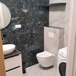 Elegancka łazienka z marmurowymi płytkami w odcieniach granatu i szarości. Umywalka nablatowa, toaleta podwieszana i pralka. Minimalistyczny design.